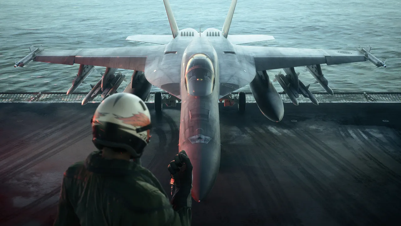 A pilot in a white helmet faces an F/A-18 fighter on a carrier deck with the sea behind it